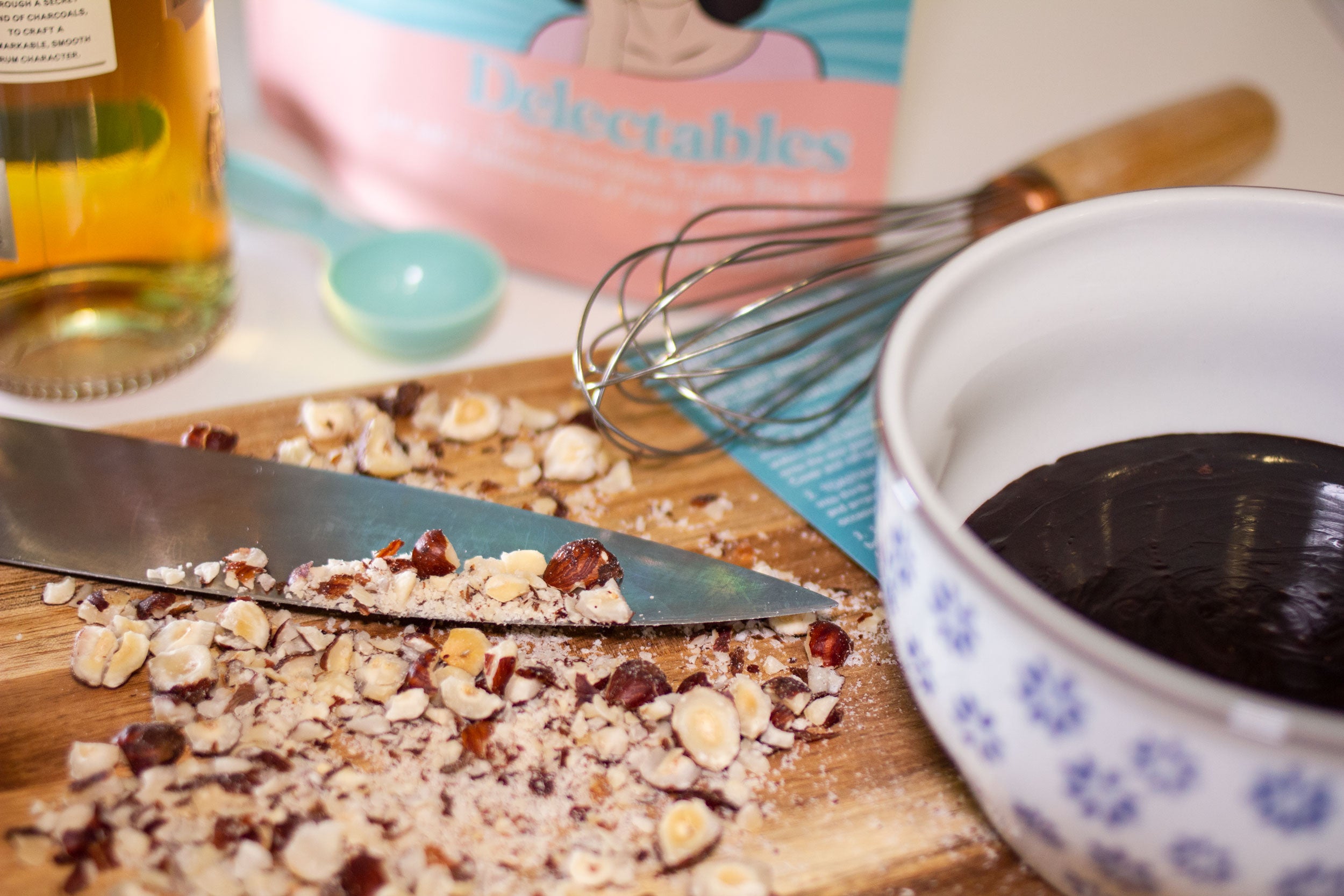 Hazelnuts on a cutting board with melted chocolate and whiskey in the background